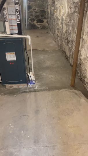 Basement utility area with concrete floor, narrow walkway, furnace, and exposed stone walls