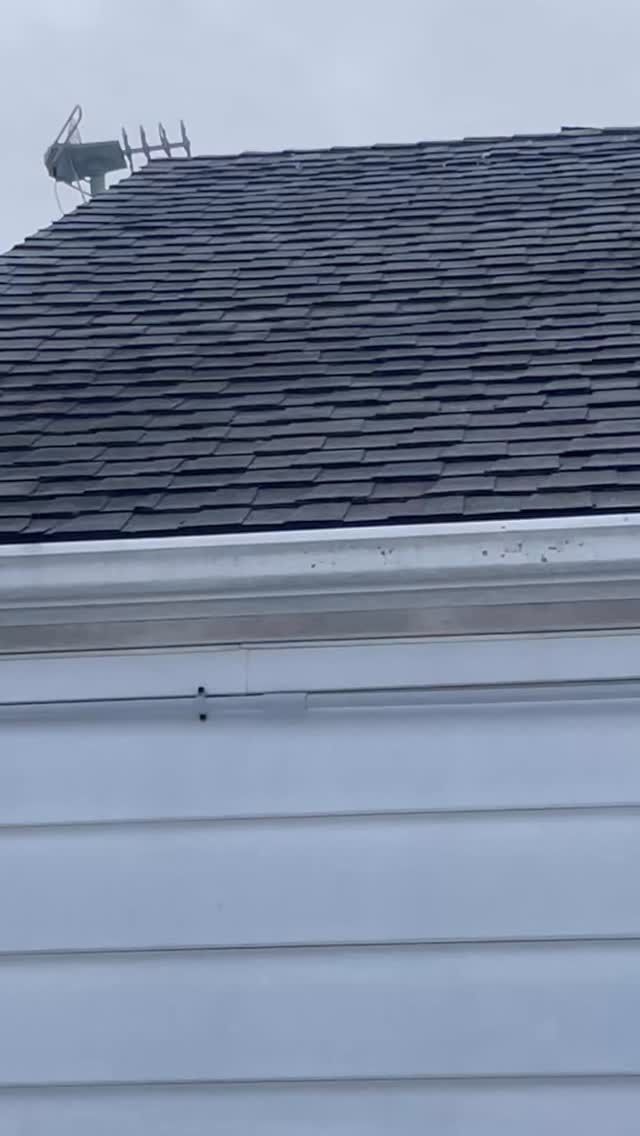 Snow-covered dark roof above white house siding