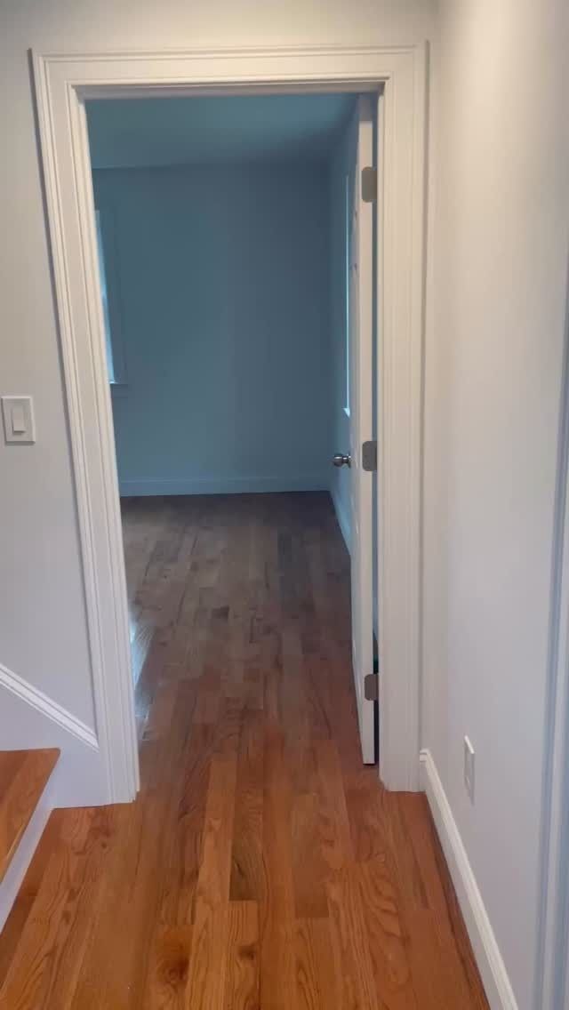 Hallway with hardwood floors leading through a white doorway into a blue-painted room