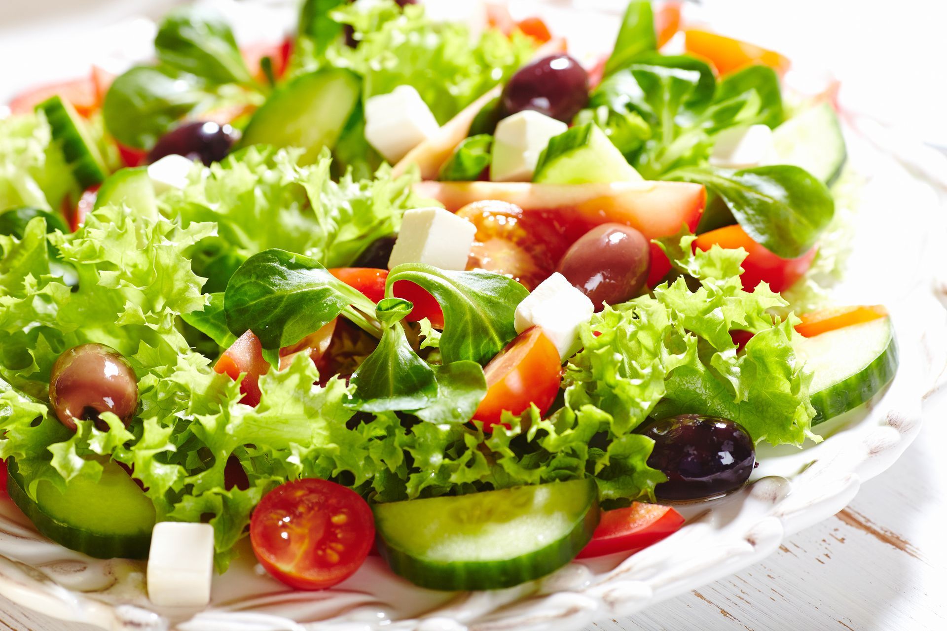A salad with lettuce , tomatoes , cucumbers , olives and feta cheese on a plate.