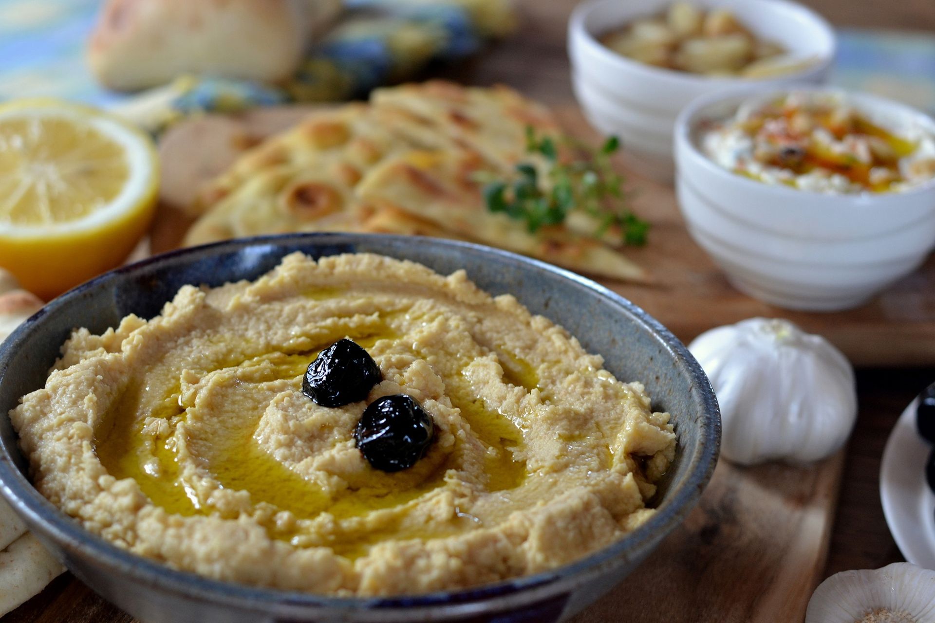 A bowl of hummus with olives on top is sitting on a wooden table.