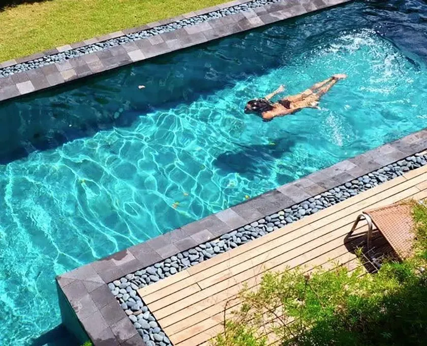 Mulher nadando estilo livre em uma piscina retangular revestida com pedras naturais.