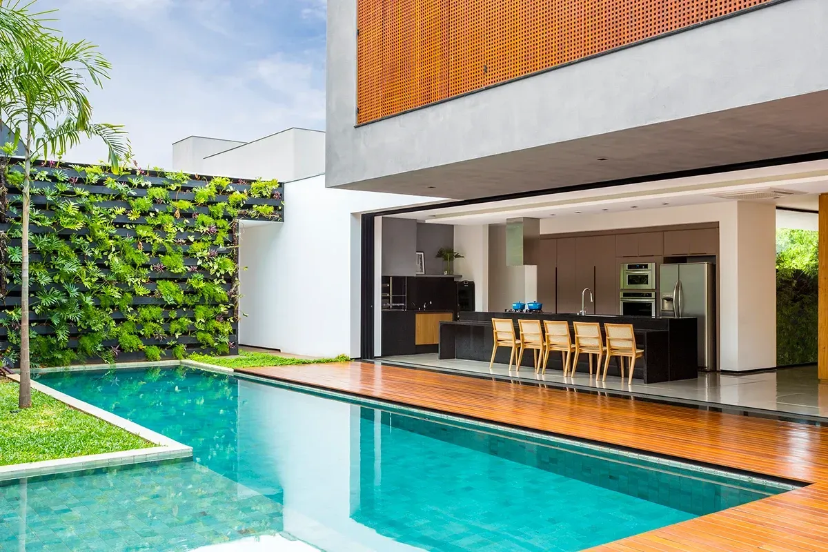 Casa moderna com piscina revestida com hijau Artemano; cozinha com balcão integrada à área externa. 