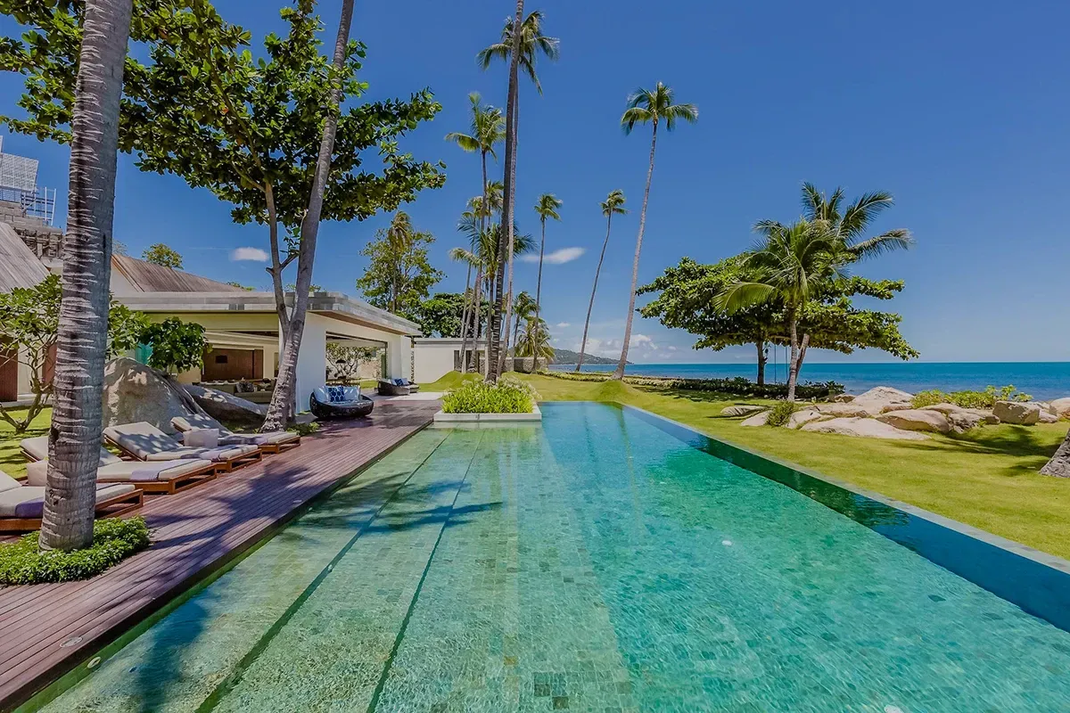 Piscina infinita revestida com hijau e vista para o oceano, palmeiras e céu azul.