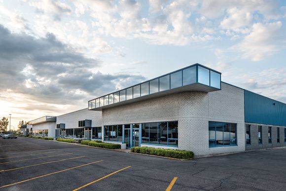 Modern, single-story office building with a paved parking lot and green landscaping at sunset.