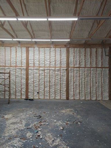 An interior view of a room under construction with white spray foam insulation between wooden wall and ceiling studs.