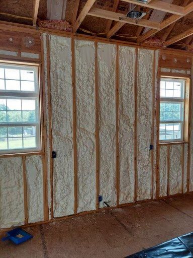 Interior wall framing and window frames filled with white spray foam insulation in an unfinished room.