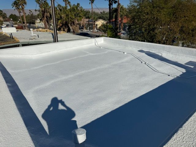 A white, freshly coated flat roof under a clear blue sky, with the silhouette of a person taking a photo visible.