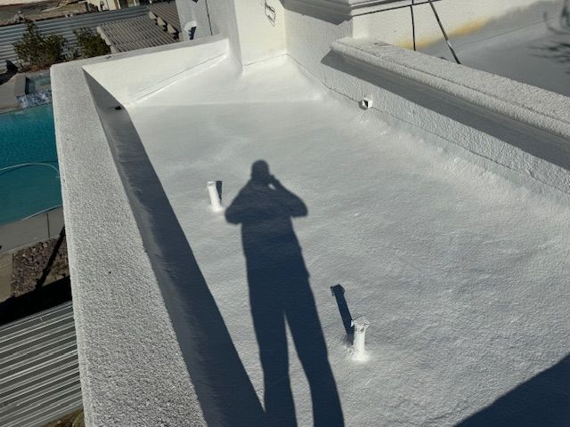 A person’s shadow cast across a freshly coated white flat roof with two small white ventilation pipes.