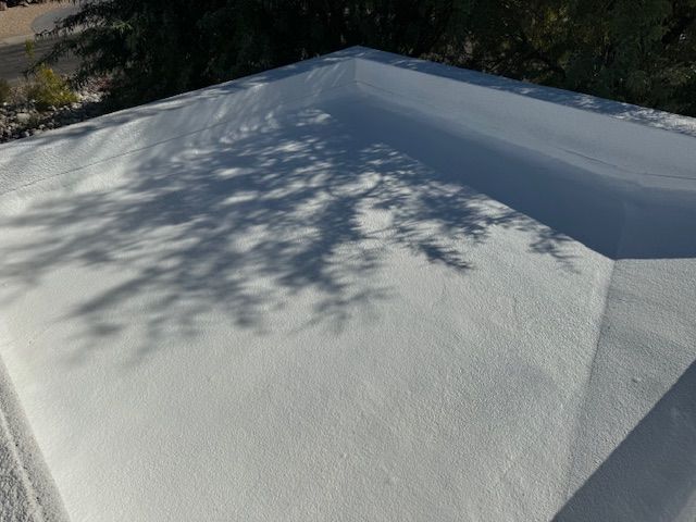 A white, flat roof surface textured with a granular coating, featuring the distinct shadow of tree branches.
