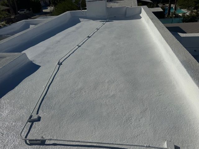 A white flat roof with a textured coating and electrical conduit piping running across the surface.
