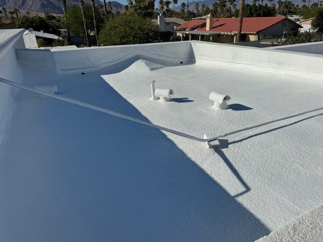 A freshly white-coated flat roof featuring two small ventilation pipes under a bright, sunny sky.