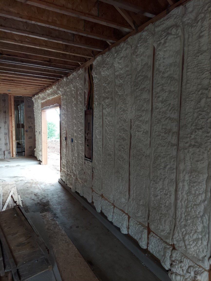 An interior view of a room under construction with spray foam insulation applied to the wall studs.