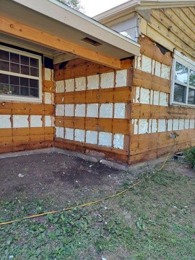 Exterior wall of a house with removed siding, revealing horizontal wooden structural beams and white insulation panels.