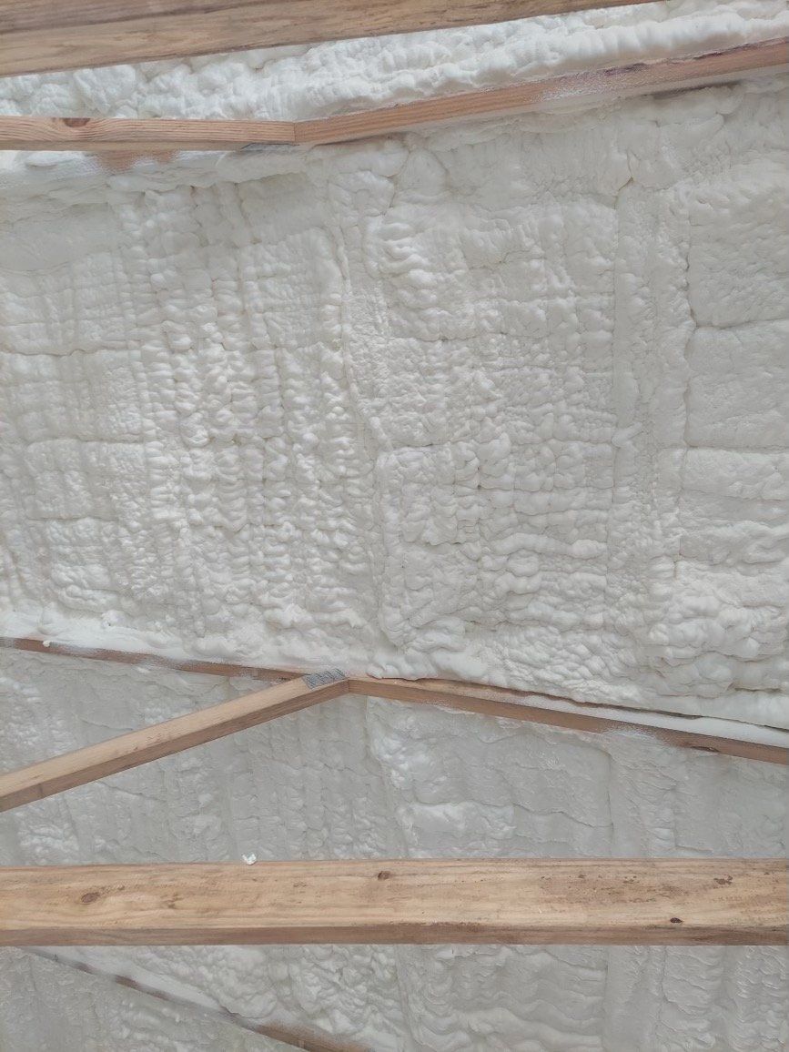 White spray foam insulation applied between wooden roof rafters and beams.