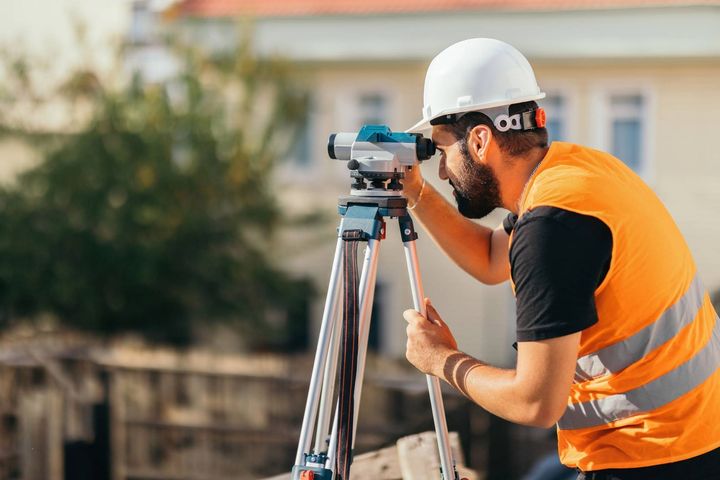 A construction worker is looking through a telescope on a tripod.