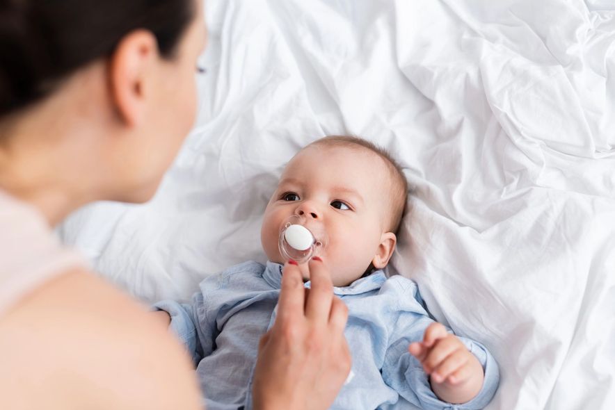 Un adulto consola un neonato con il ciuccio su un letto bianco.
