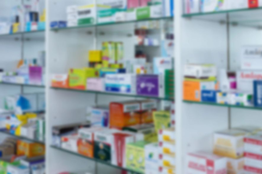 Scaffali di farmacia sfocati, pieni di scatole e flaconi di medicinali colorati.