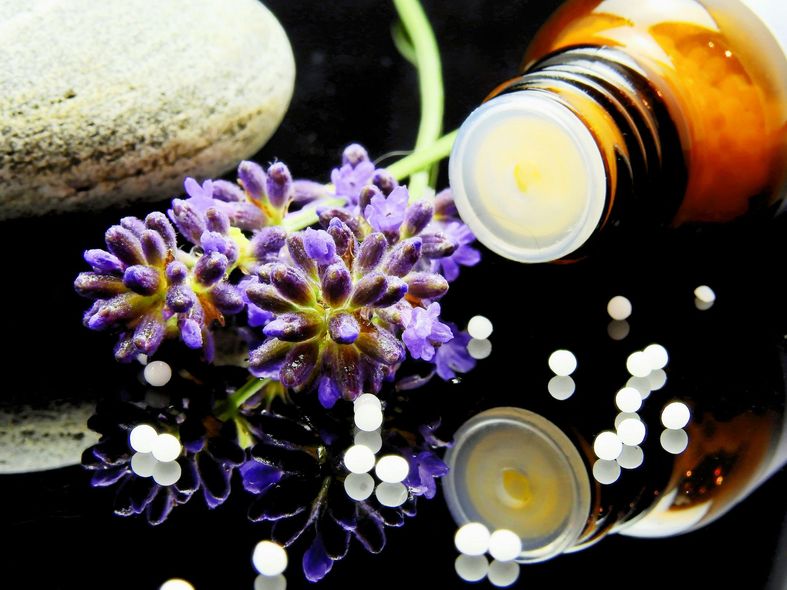 Flaconi di profumo color ambra e fiori viola su una superficie nera riflettente con una pietra bianca