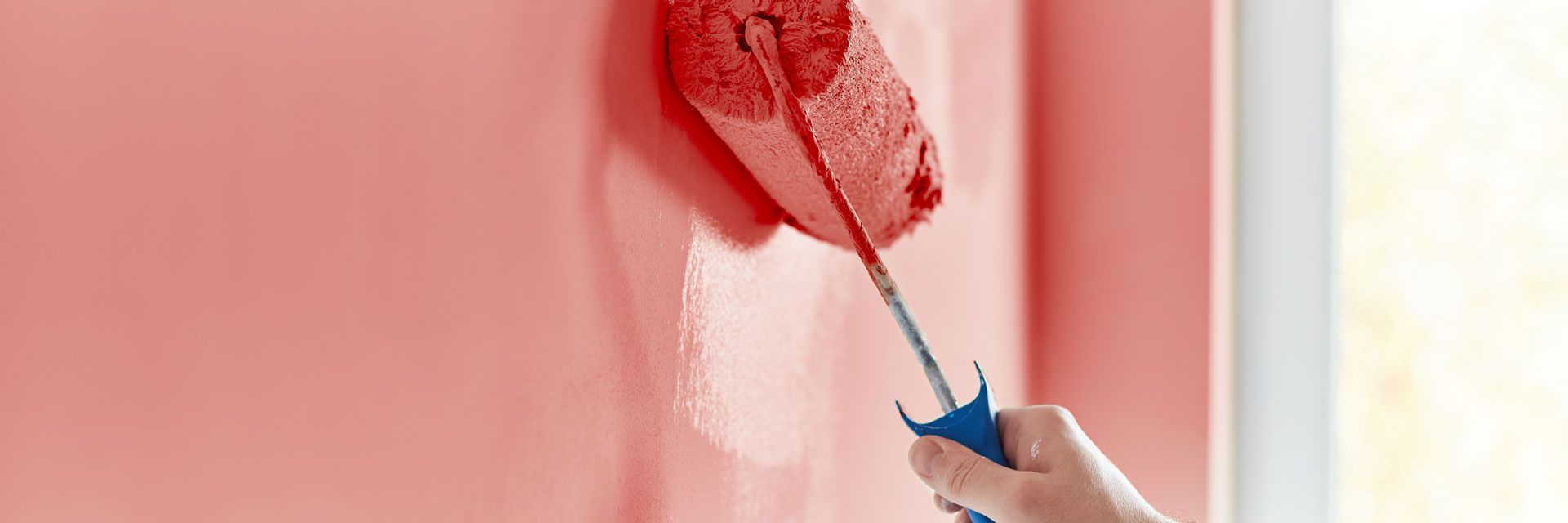 Person paints a wall with a red roller, leaving a red stripe on a pink surface.