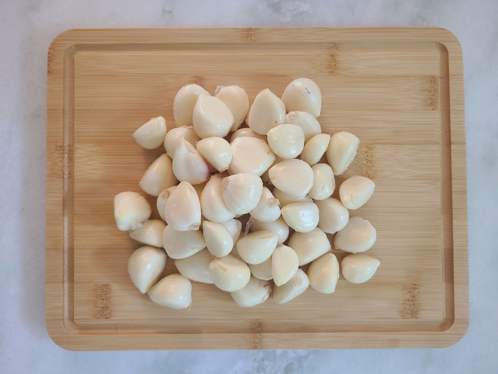 A pile of peeled garlic cloves on a wooden cutting board.