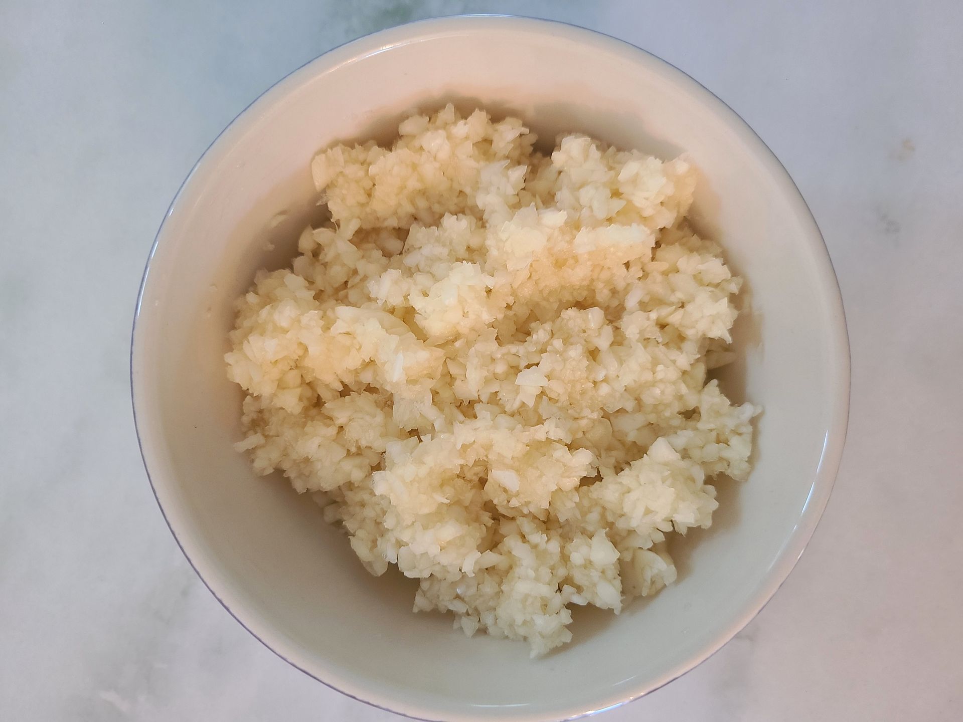 A white bowl filled with chopped garlic on a light surface