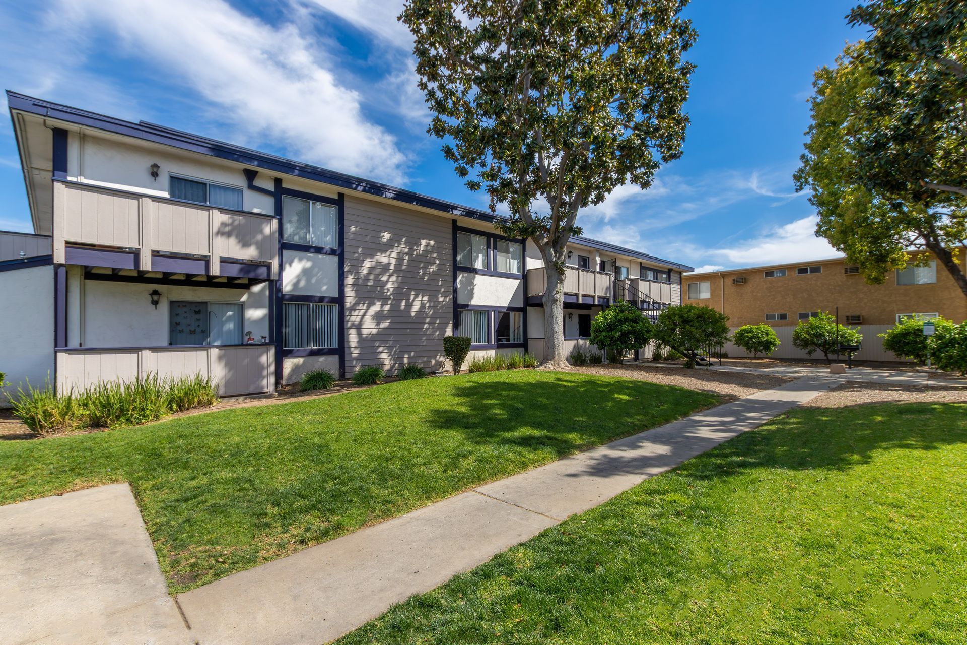 Apartment complex courtyard with green lawn, sidewalks, trees, and blue sky