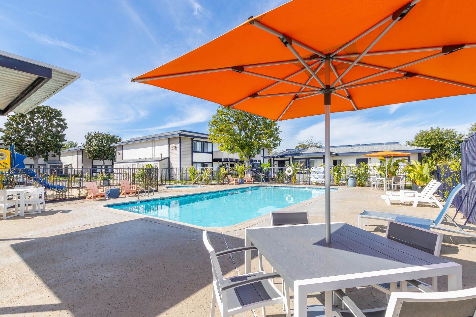 Outdoor resort pool with orange umbrellas and lounge chairs beside a patio table