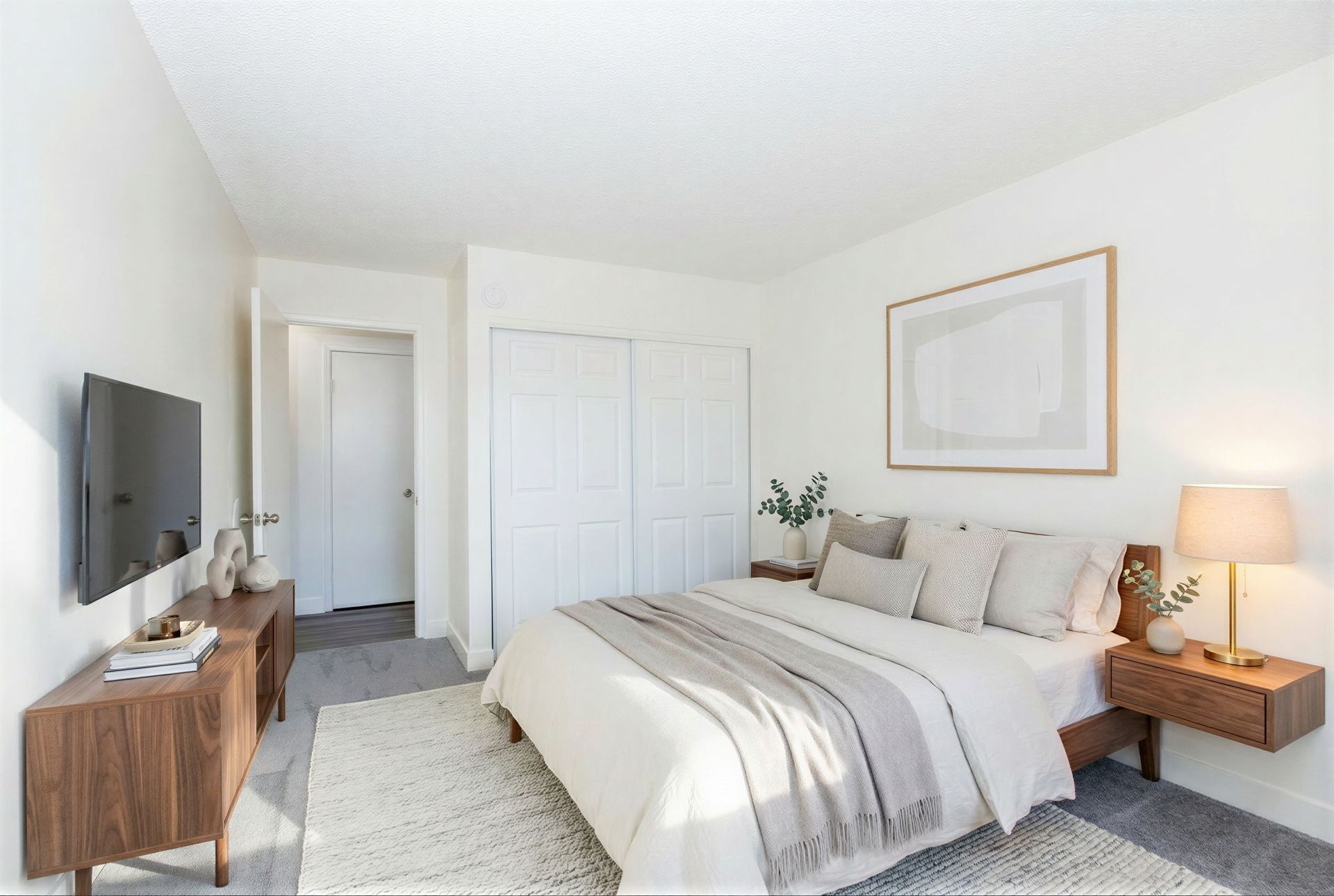 Bright bedroom with a bed, wall-mounted TV, dresser, and bedside lamp in neutral tones