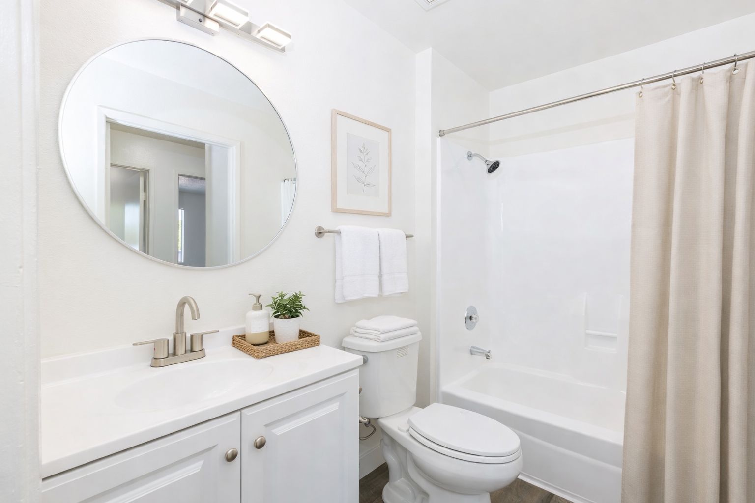 Bright white bathroom with round mirror, vanity, toilet, and tub with shower curtain