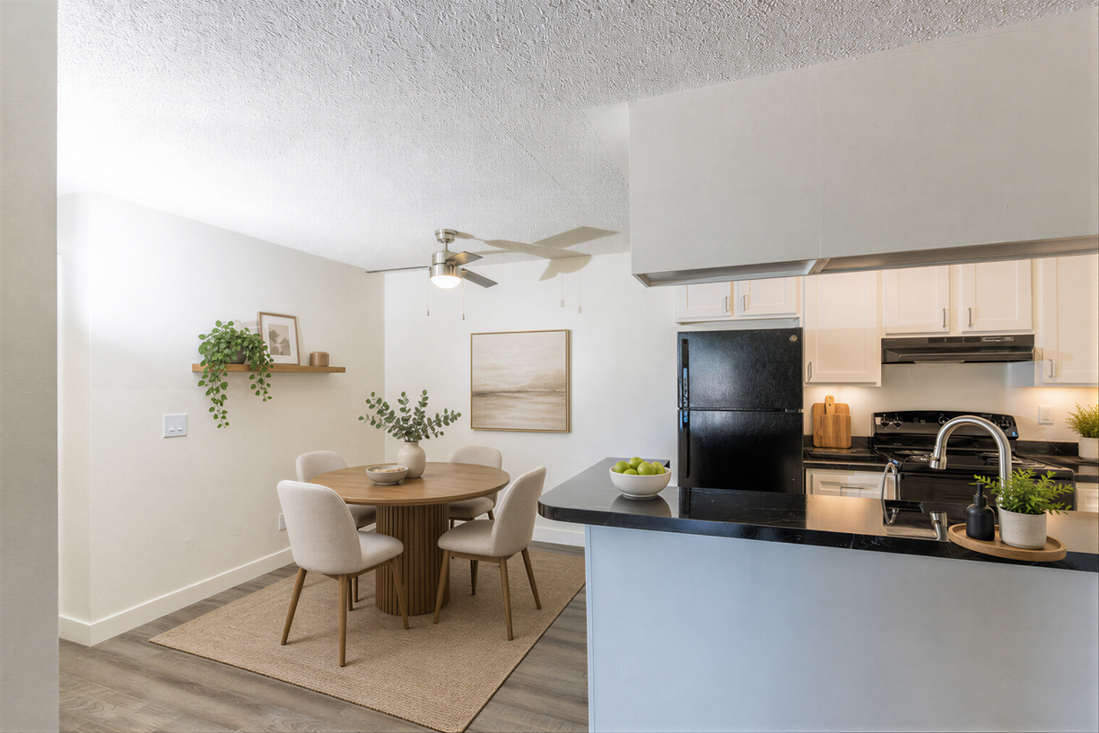 Bright open dining area beside a modern kitchen with white chairs, round table, and black island counter.