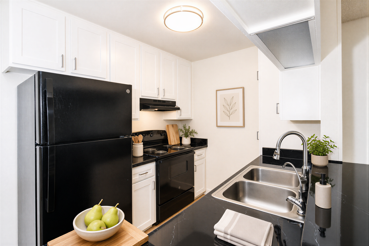 Modern white kitchen with black appliances, stainless sink, and a bowl of green apples on the counter