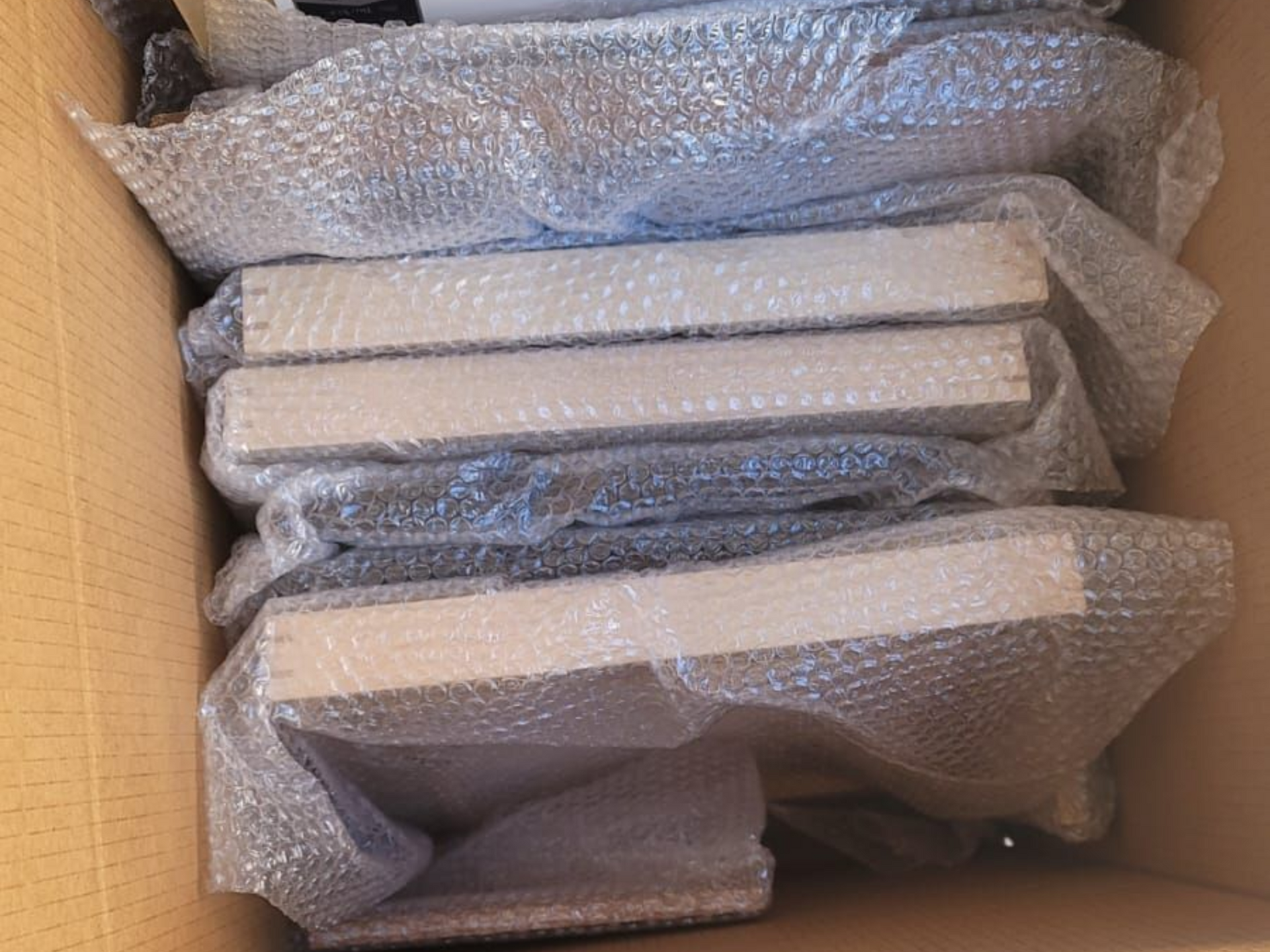A cardboard box containing several rectangular wooden boards wrapped in bubble wrap for protection.