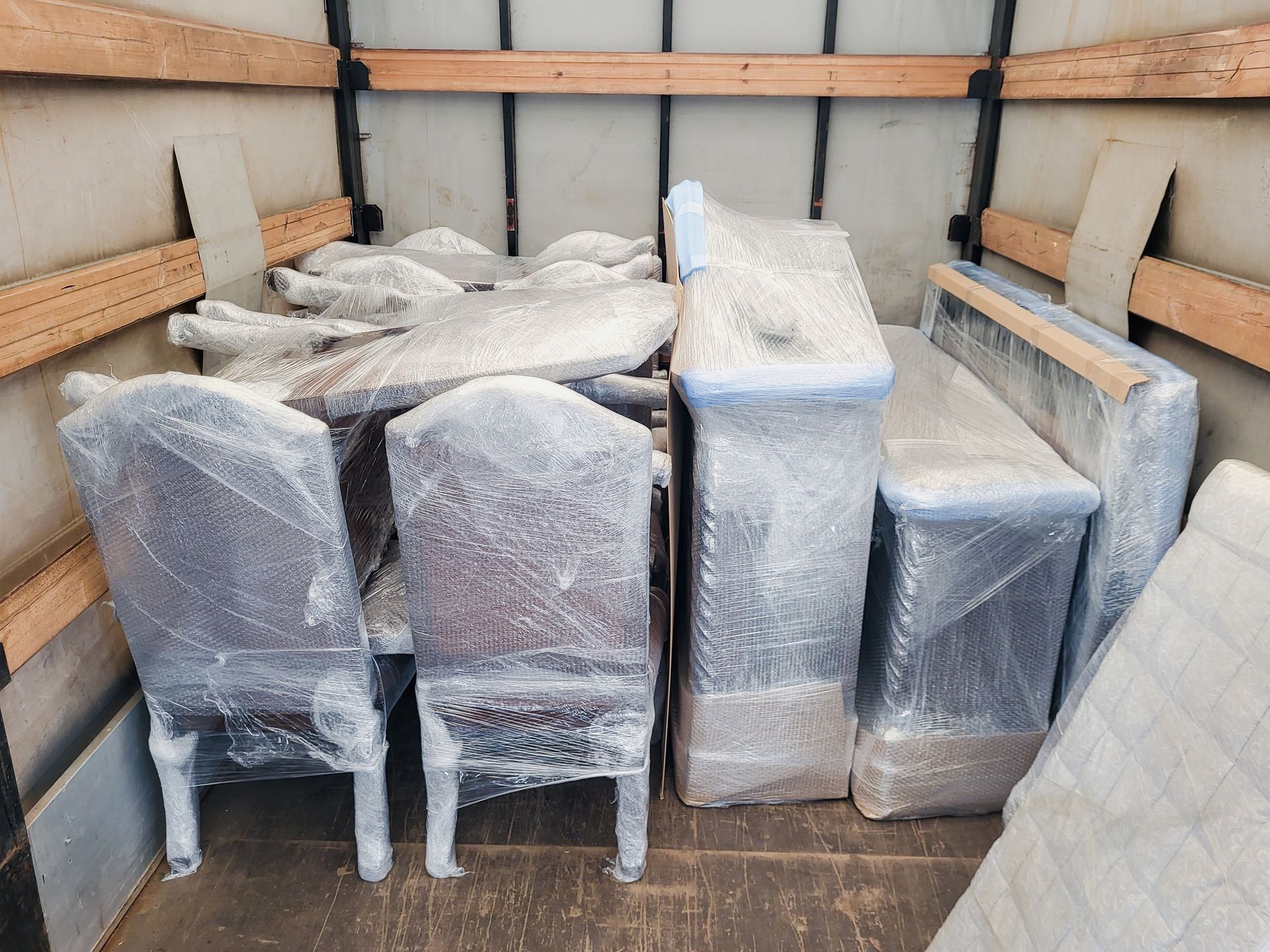 Wrapped furniture items stacked in a truck bed, covered in clear plastic and moving blankets.