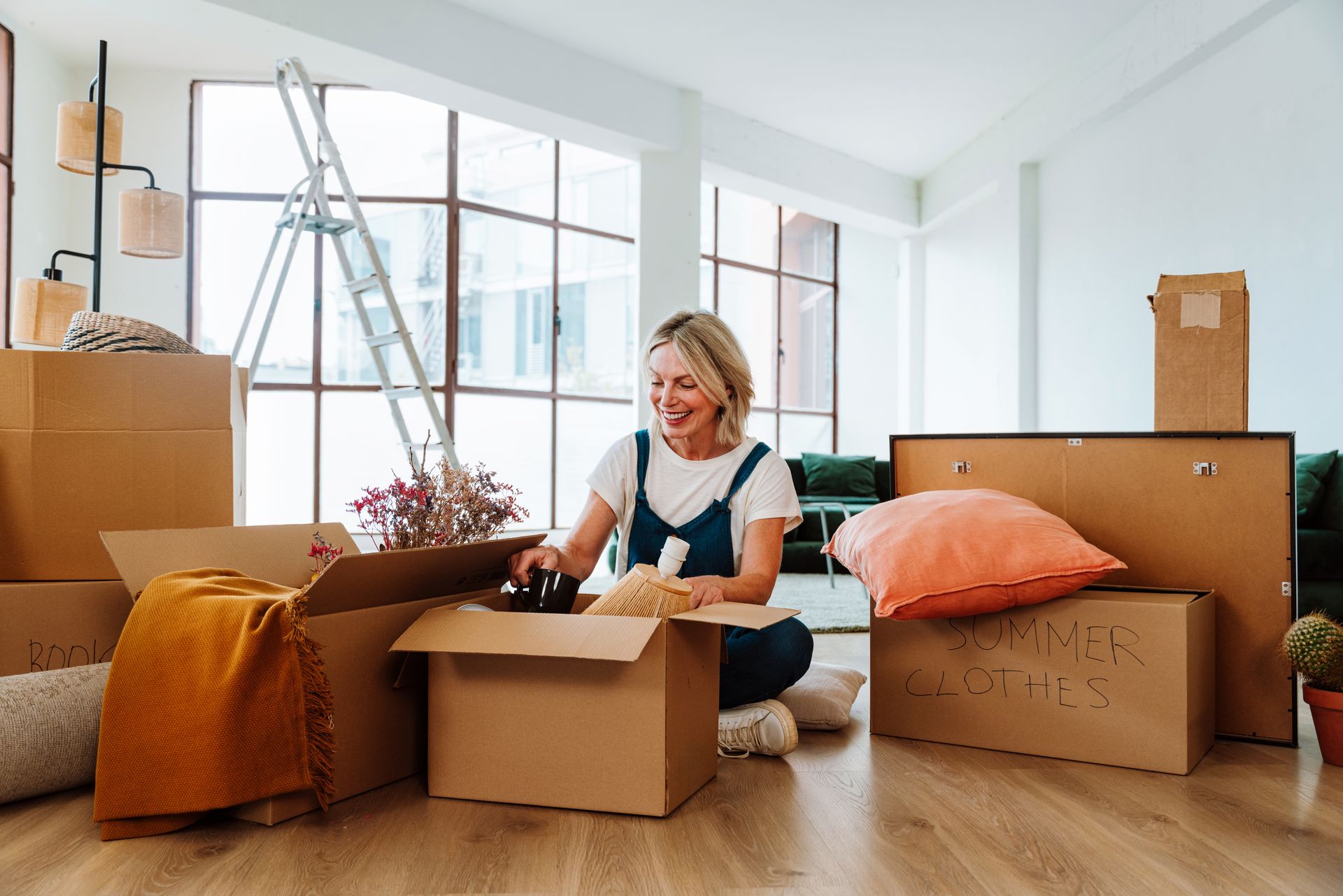Person packing boxes in a bright room with a ladder and moving supplies