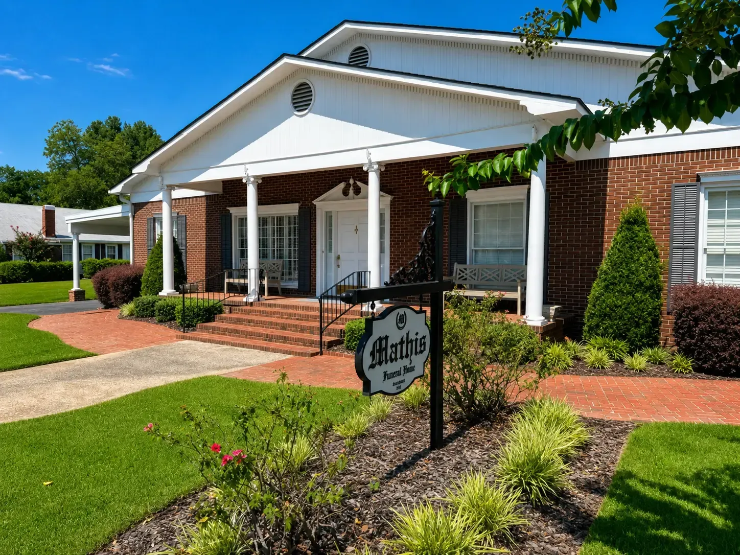 Single-story brick house with white porch, trimmed lawn, and landscaped flower beds