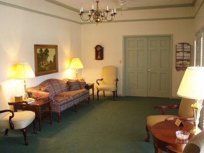 Cozy living room with green carpet, sofa, armchairs, lamps, and double doors