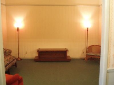 Empty living room with green carpet, low wooden table, and warm wall lamps on both sides