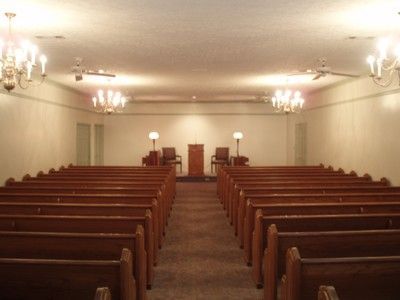 Empty church sanctuary with rows of wooden pews facing the altar and chandeliers overhead