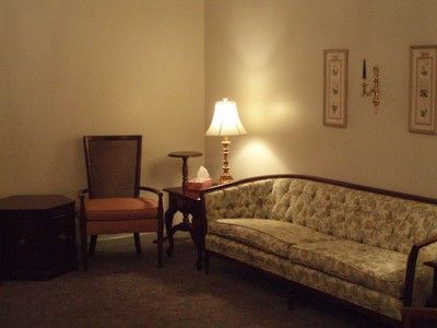 Cozy living room corner with a floral sofa, chair, side table, and lit lamp against cream walls.
