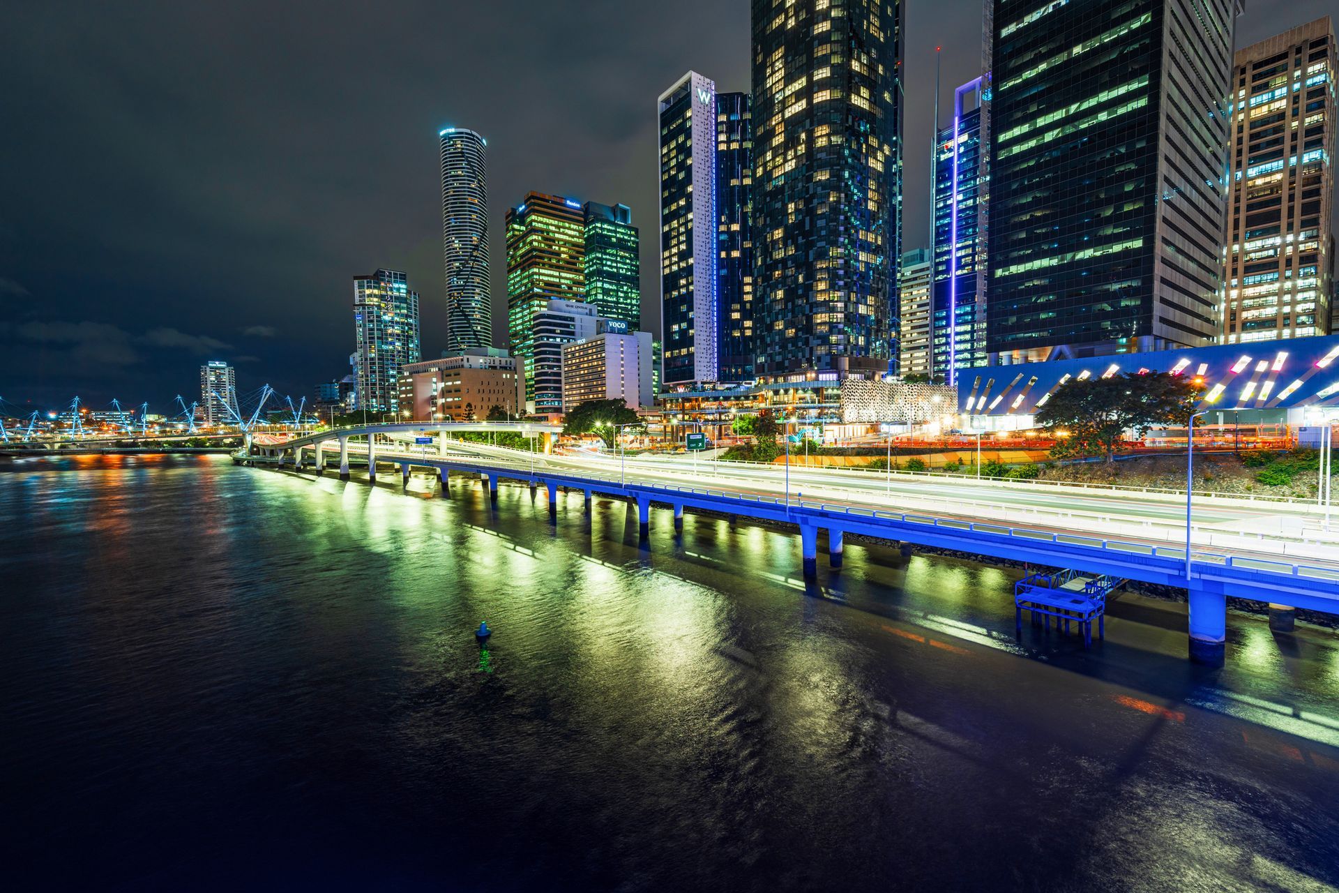 A bridge over a body of water with a city skyline in the background at night.