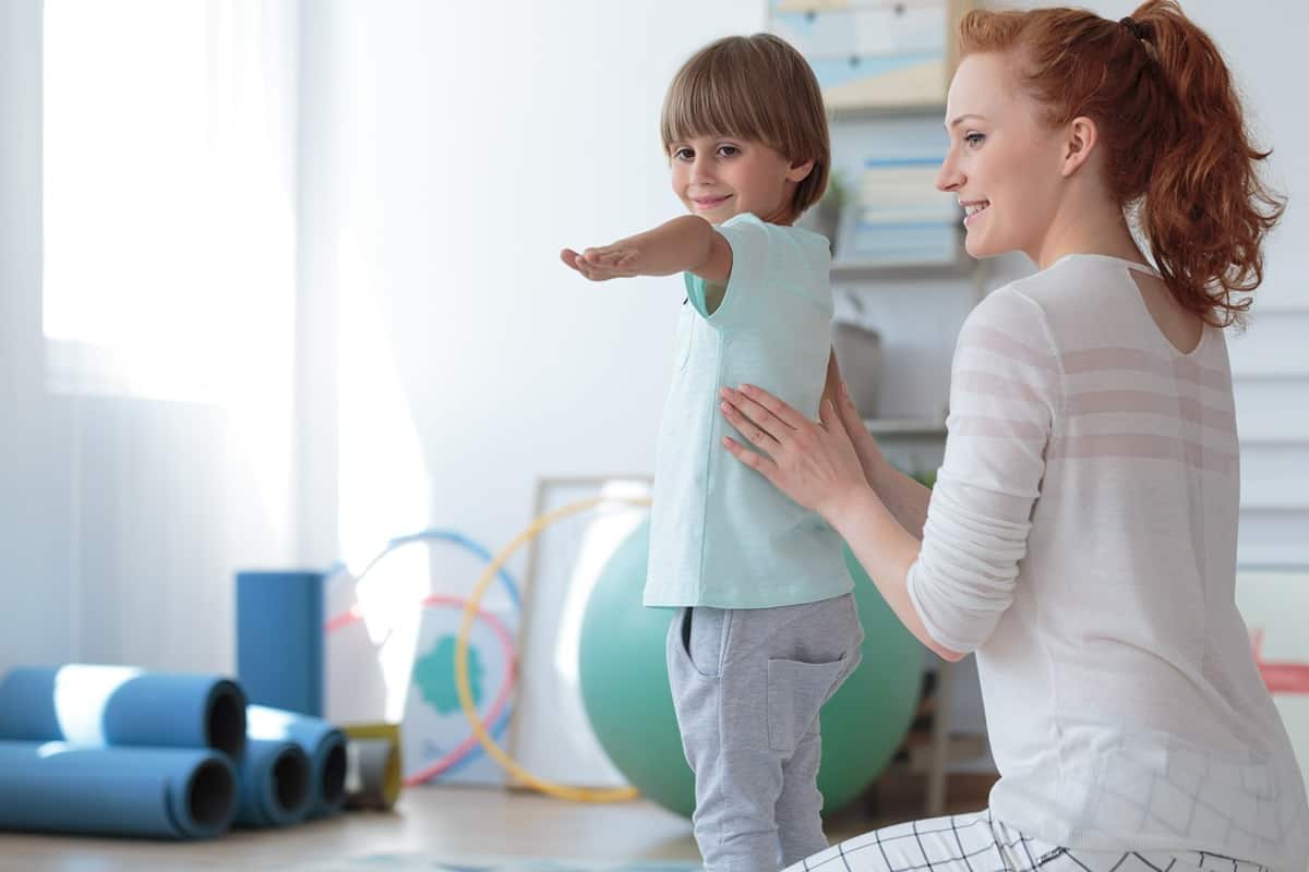 A physical therapist helps a child stand up straight near balance balls near Richmond, Kentucky (KY)