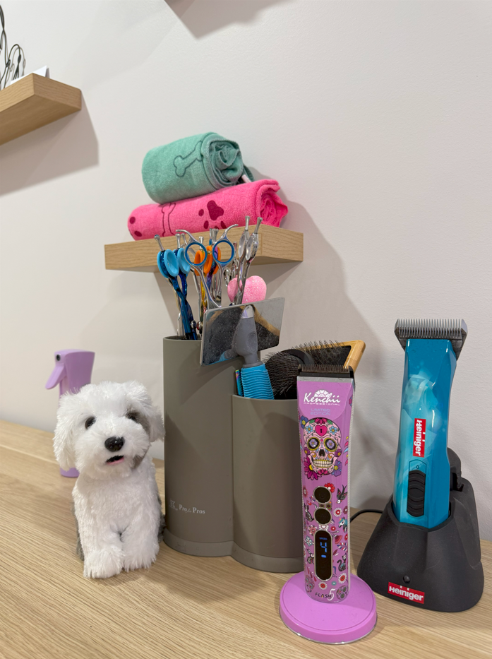 A small white dog toy is sitting on a wooden table next to dog grooming clippers.