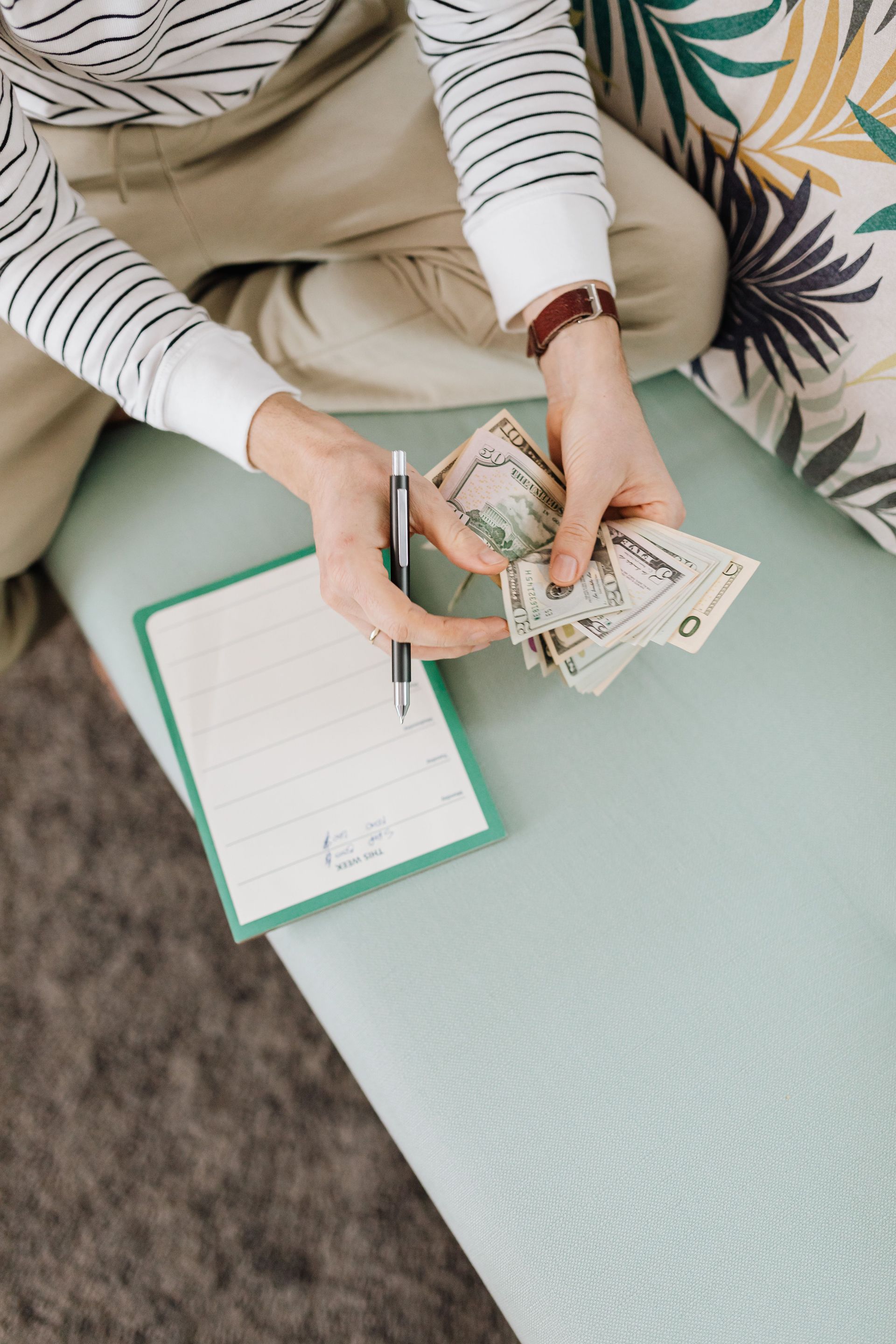 Hands counting cash beside a clipboard on a mint green table