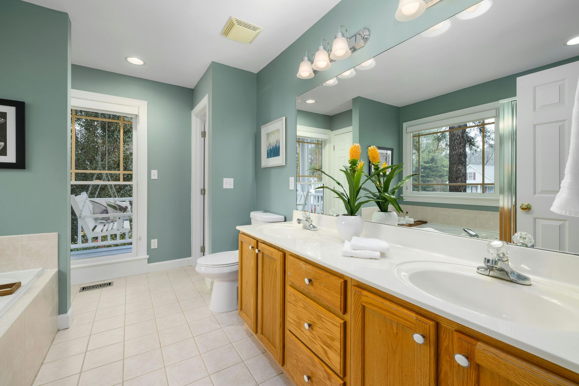 A bathroom with soft sage-green walls, a large wooden vanity with a white countertop, and a tiled floor.