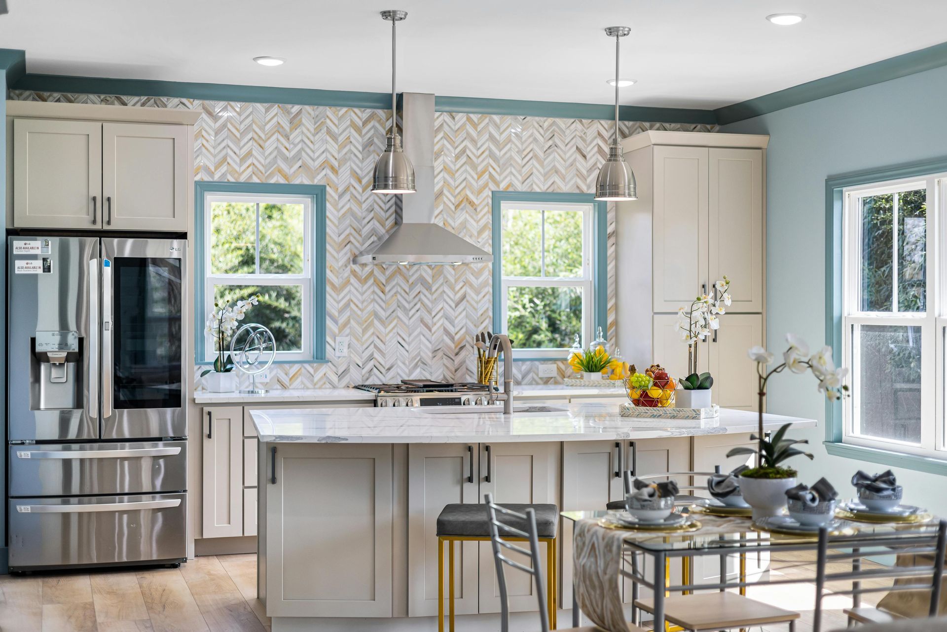 A modern, bright kitchen featuring a white island, light gray cabinets, stainless steel appliances, and herringbone tile.