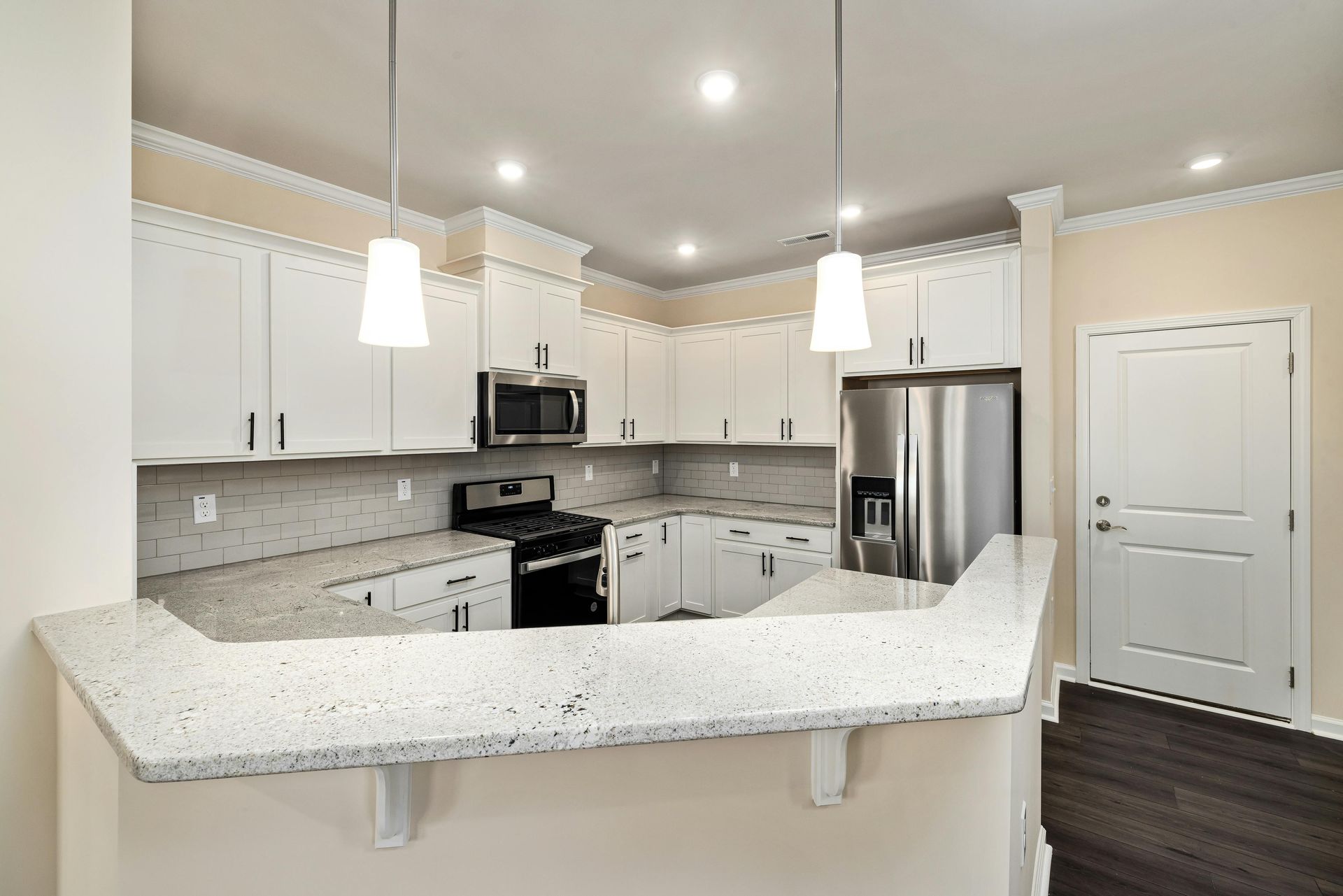A kitchen with white cabinets, speckled granite countertops, stainless steel appliances, and a breakfast bar.
