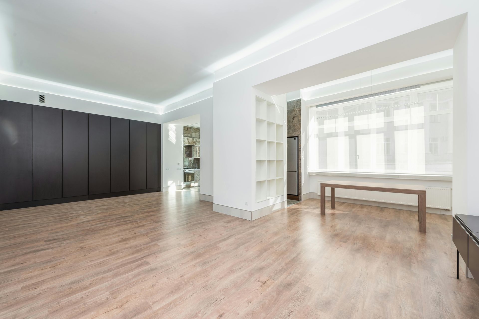Empty modern room with dark cabinetry, light wood floors, and large window.