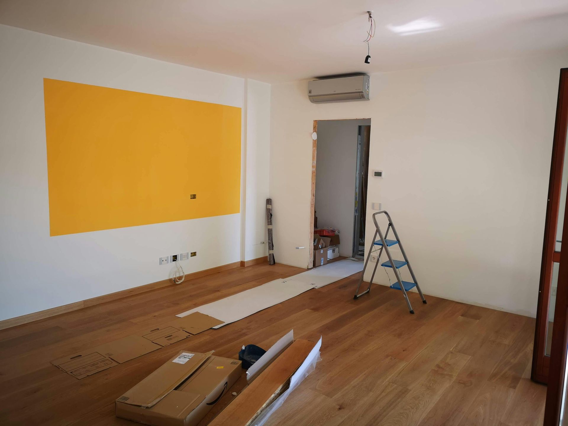 Room with wood floor, yellow painted wall section, doorway with ladder, and boxes.