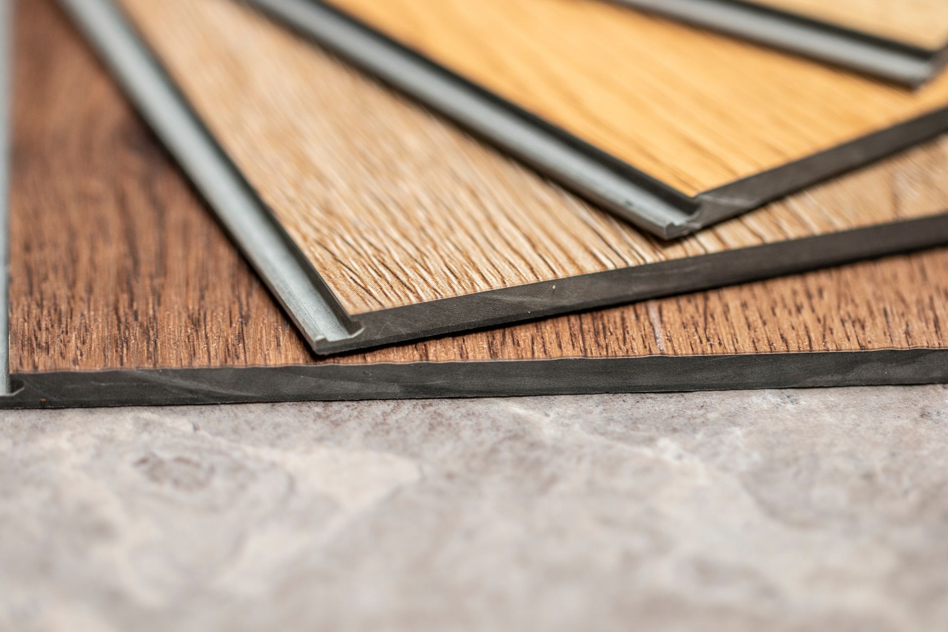 Close-up of wood-look flooring samples in shades of brown and tan, stacked on a gray surface.